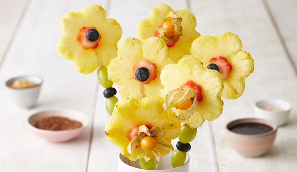 Six Fruit Flower Fondue Sticks served in a cup, with dipping sauces in the background