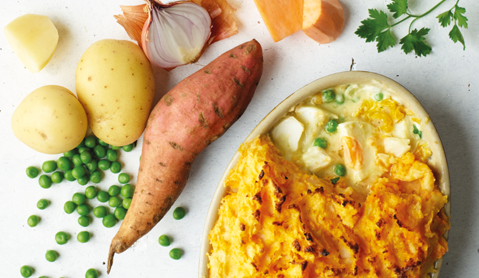 Smoked Fish Pie with Sweet Potato Topping with a portion missing to see the filling, placed next to various vegetables used in the recipe